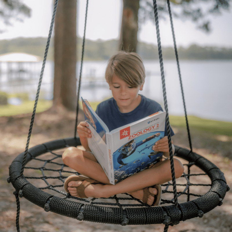 Homeschool student reading Zoology on a backyard swing