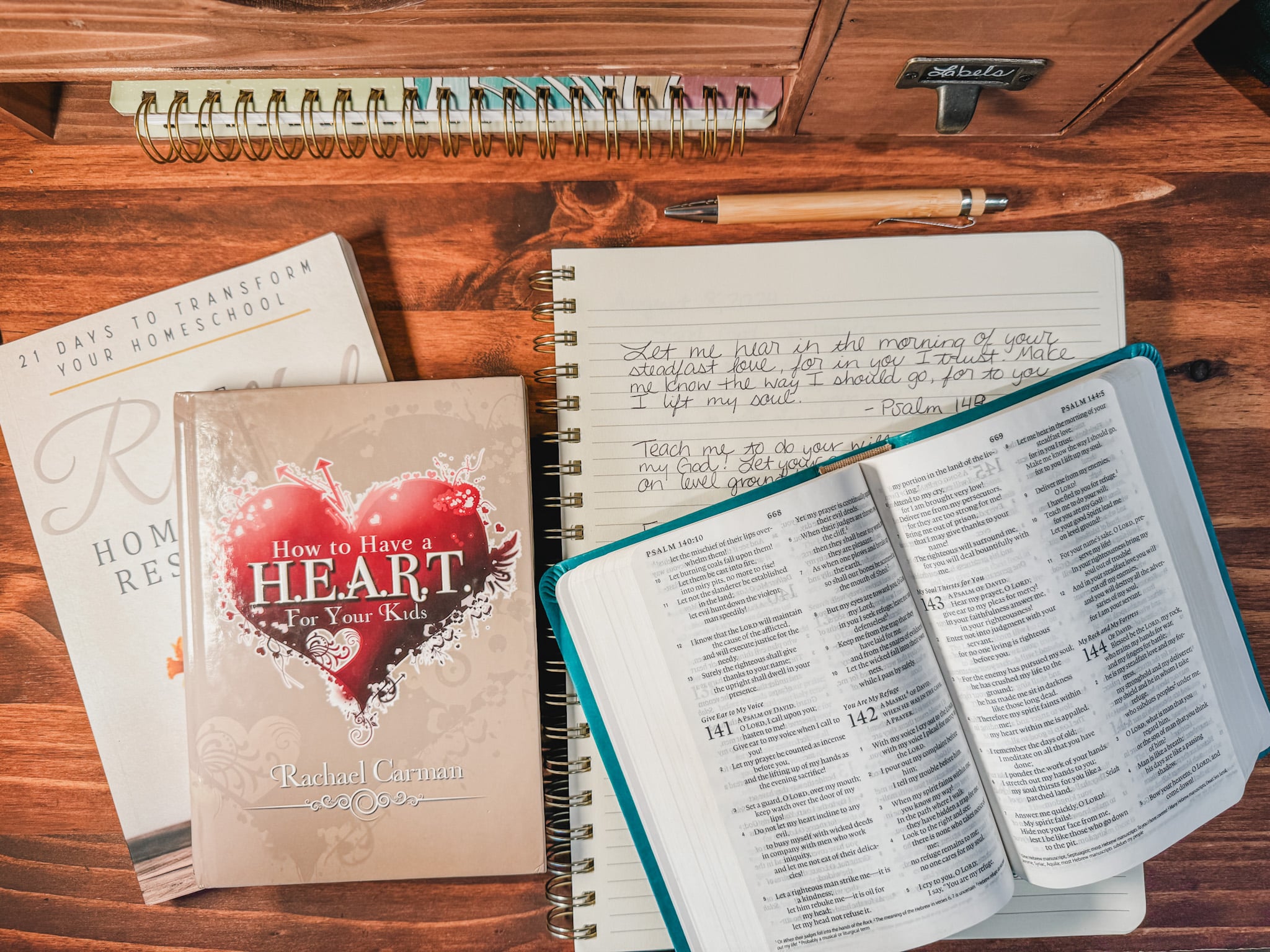 How to Have a H.E.A.R.T for Your Kids book by Rachael Carman with open bible, notebook, another book, and a pen sitting on a desk