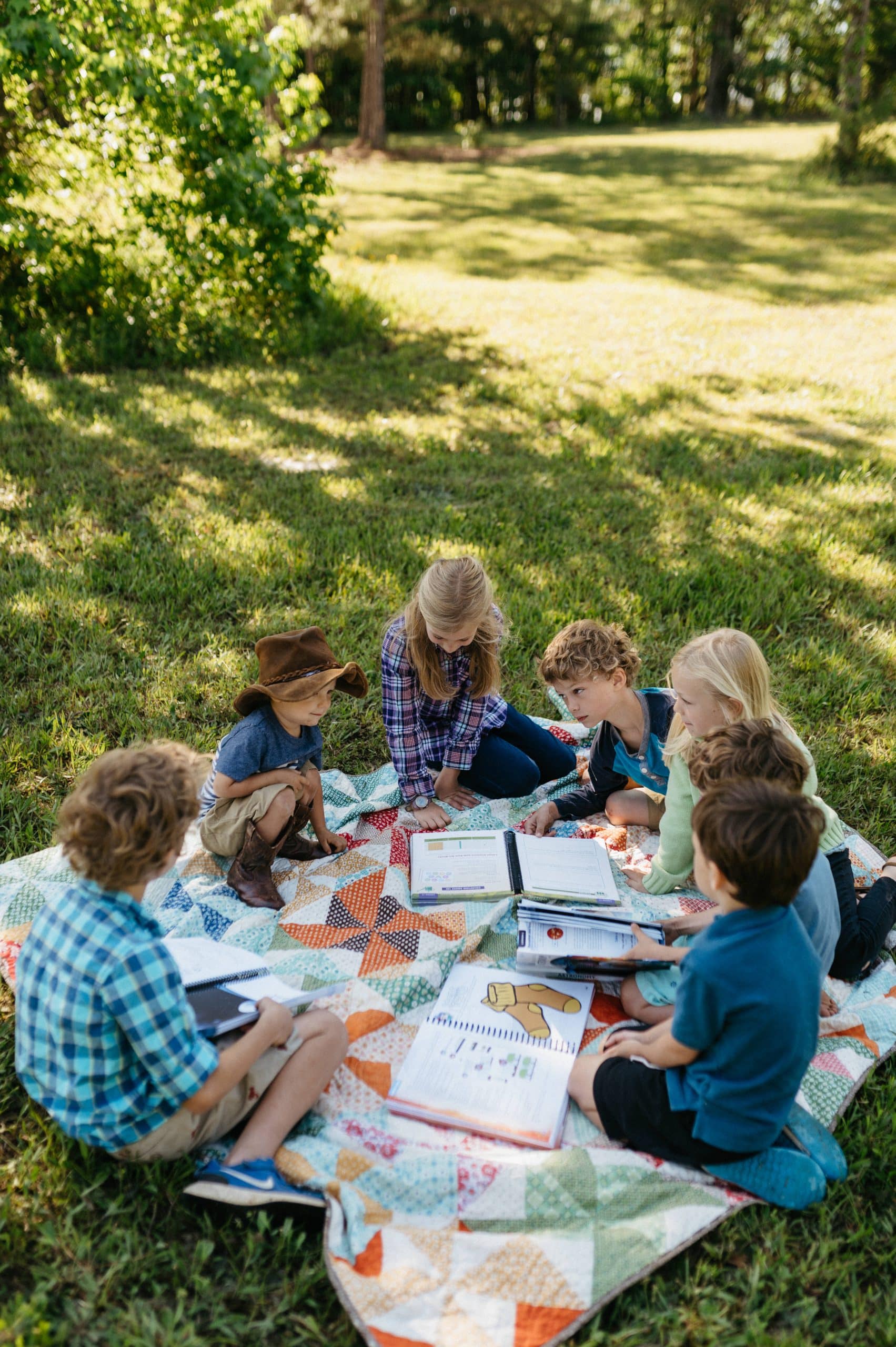 6 kids reading on a picnic blanket outside