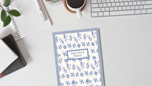 2025-2026 Homeschool Planner sitting on a desk with a plant, pen and notepad, coffee, and keyboard
